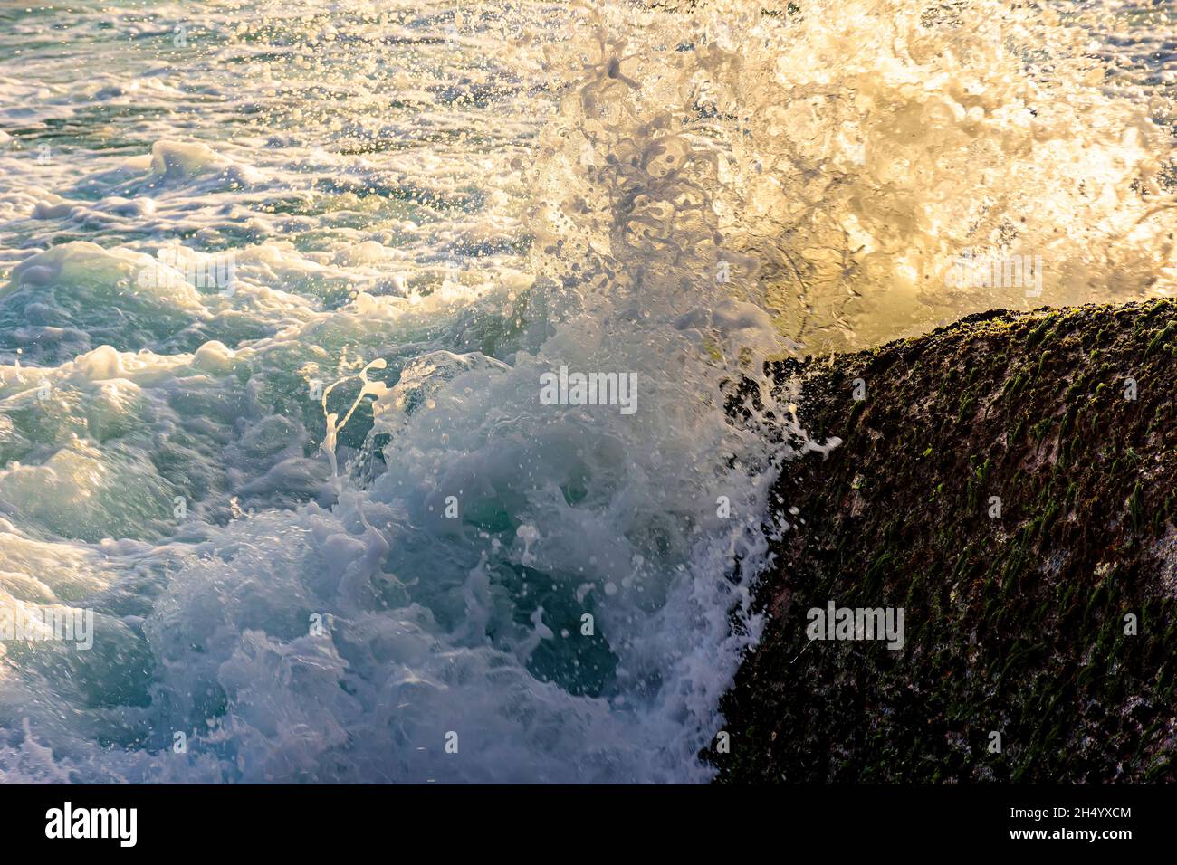 El agua y la espuma del mar salpican con las olas chocan contra las rocas  durante la puesta de sol tropical Fotografía de stock - Alamy