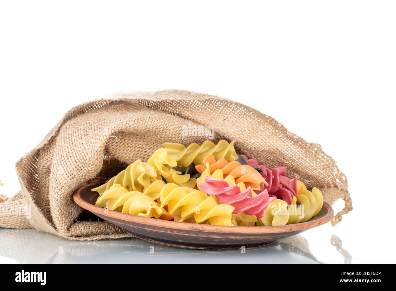 Pasta fusilli de colores crudos con bolsa de yute, primer plano, aislada sobre blanco. Foto de stock