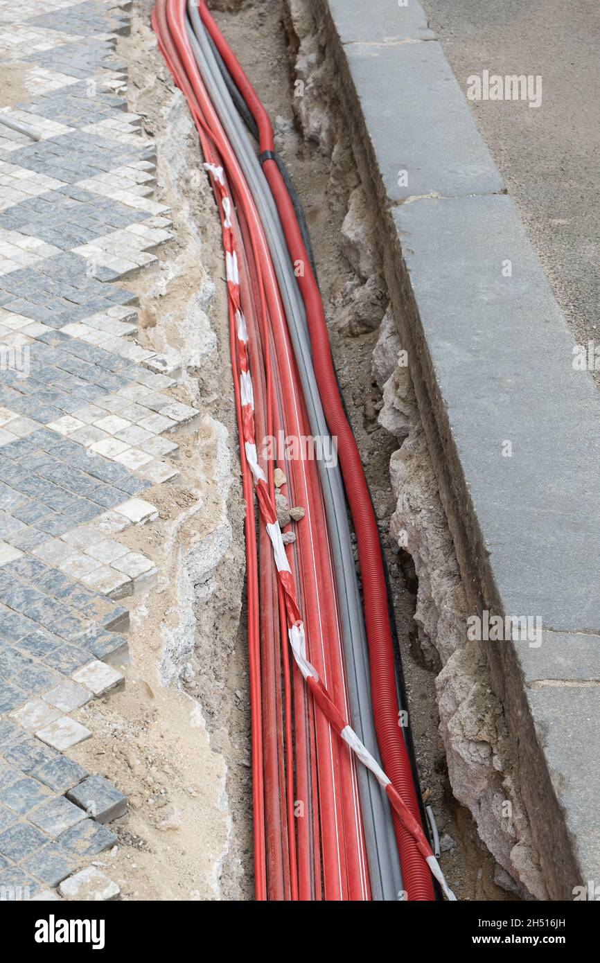 Un gran número de cables eléctricos y de alta velocidad de la red de  Internet en el tubo corrugado rojo están enterrados bajo tierra en la calle  cubierta de adoquines Fotografía de