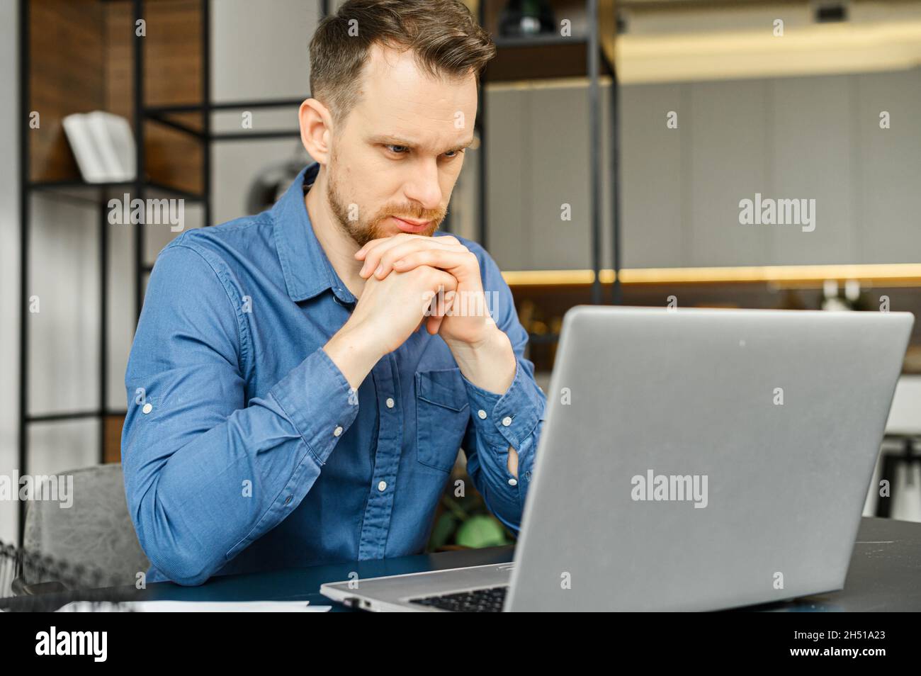 Hombre de negocios guapo que busca resolver las tareas de negocios, hombre  con camisa elegante sport con portátil sentado en el escritorio, mira la  pantalla pensativo, independiente pendiente de inspiración y nuevas