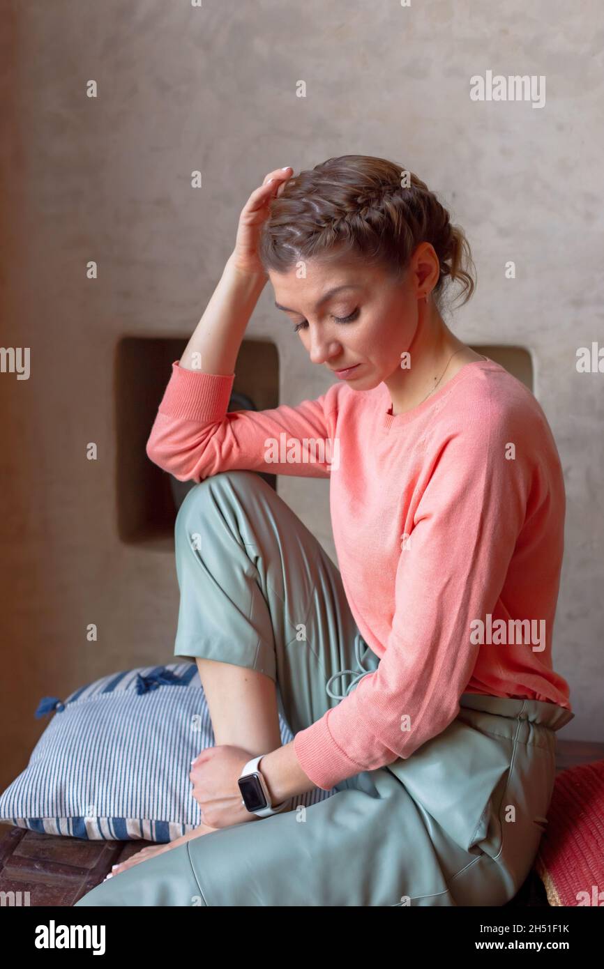 retrato hermosa mujer en sudadera de coral y pantalones grises está sentada en la habitación Foto de stock