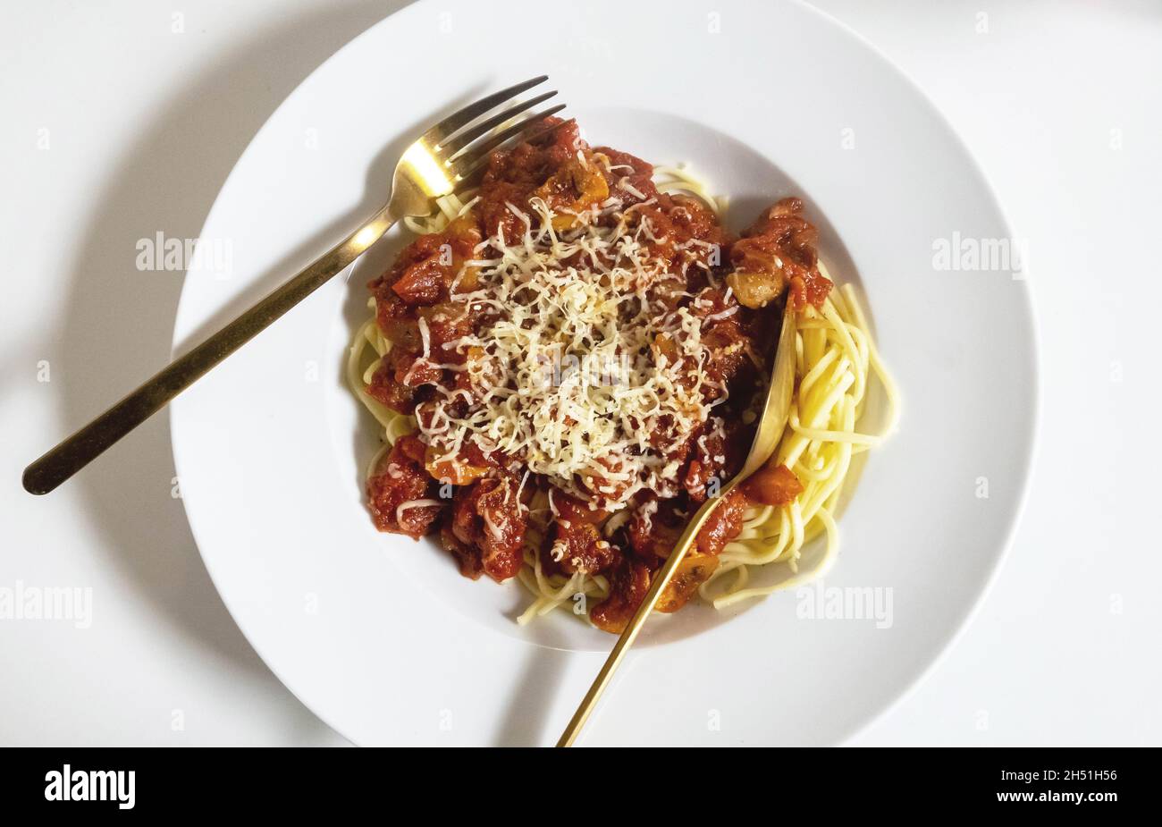 Espaguetis en un tazón blanco con una salsa de tomates San Marzano, champiñones y tocino. Tenedor y cuchara de oro. Foto de stock