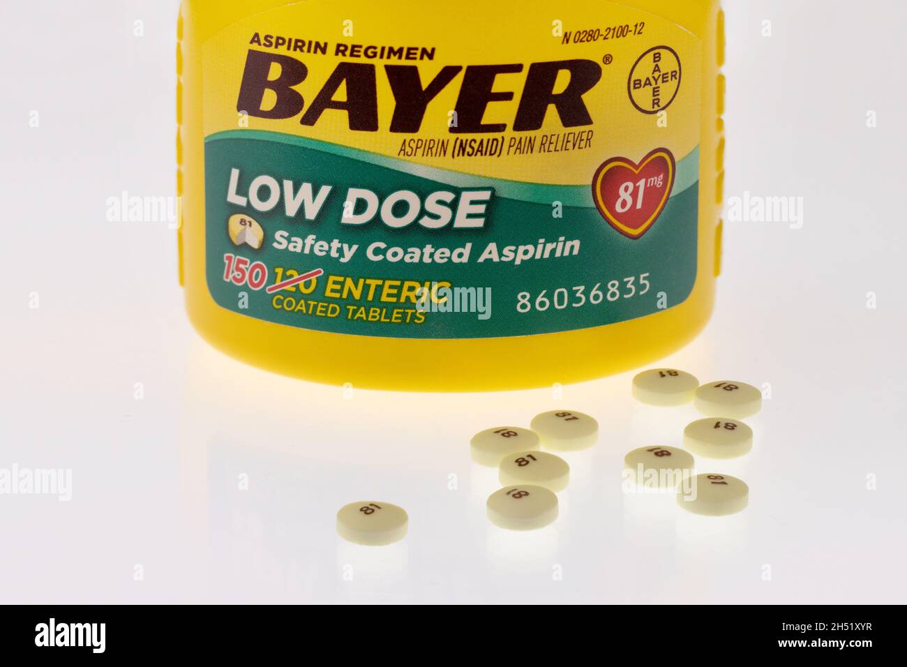 Editorial ilustrativa de la botella de aspirina en dosis bajas de Bayer y las píldoras sobre un fondo blanco reflectante. Foto de stock