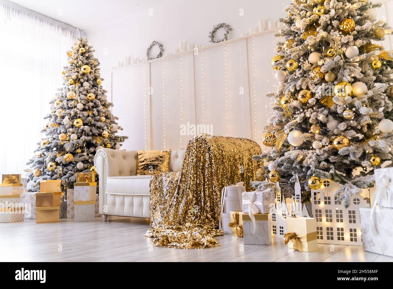 Moderno interior de Navidad blanco con dos árboles de Navidad decorados,  textil dorado, regalos dorados Fotografía de stock - Alamy