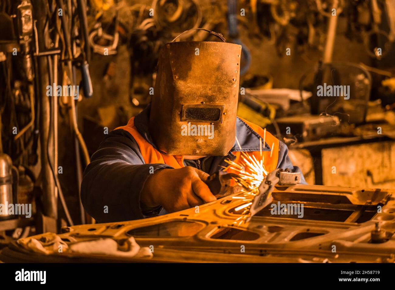 El trabajador de la soldadora en una máscara protectora de hierro repara la  puerta del coche y se dedica a trabajos de soldadura en el taller de la  planta industrial Fotografía de