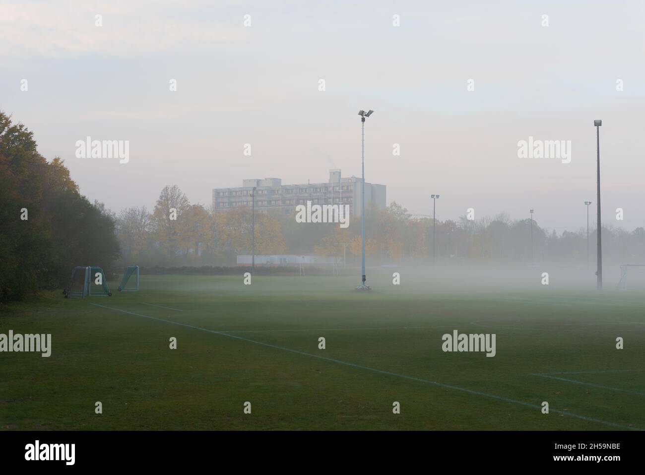 Campo de fútbol vacío y desierto en la zona suburbana con goles e inundar postes de luz en el día gris nublado con niebla y niebla Foto de stock
