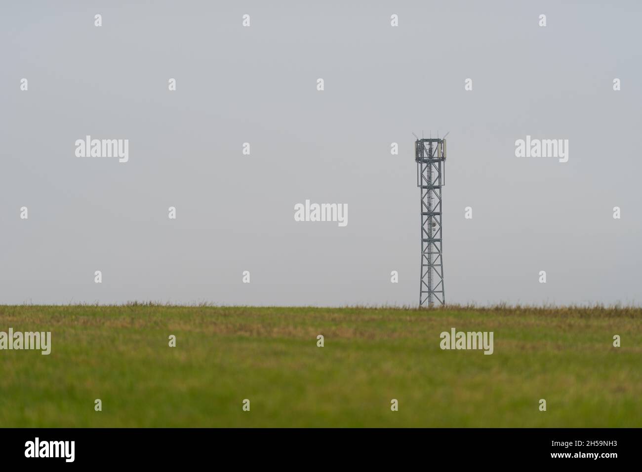 Mástil de antena de torre celular móvil que proporciona conexión móvil a Internet para el área rural que se encuentra en un campo estéril vacío en un día de color gris oscuro y oscuro Foto de stock