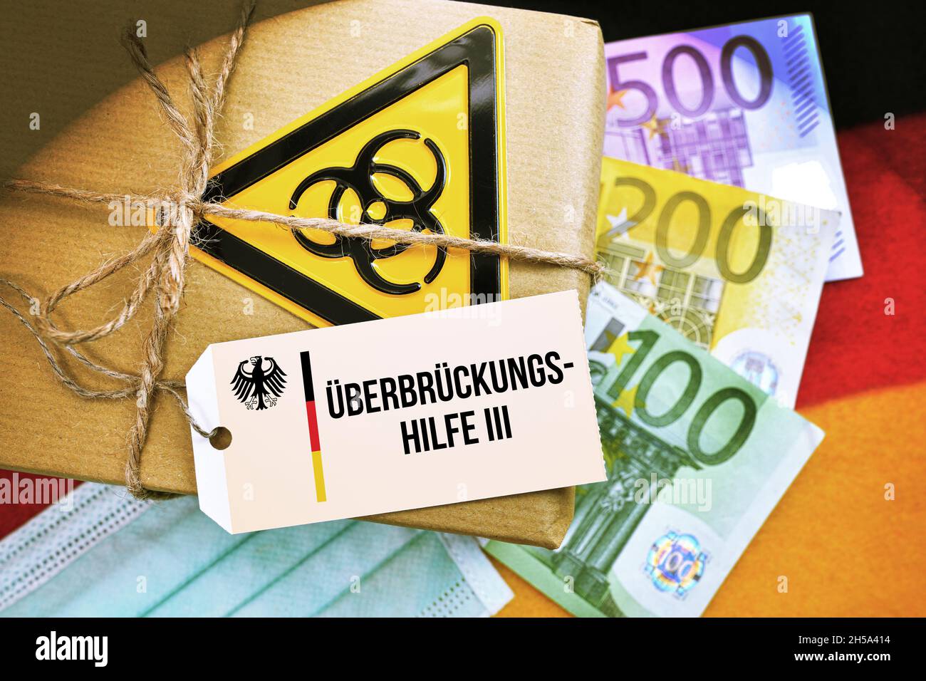 FOTOMONTAGE, Paket mit Biogefährdungszeichen auf Deutschlandfahne mit Etikett und der Aufschrift Überbrückungshilfe III Foto de stock