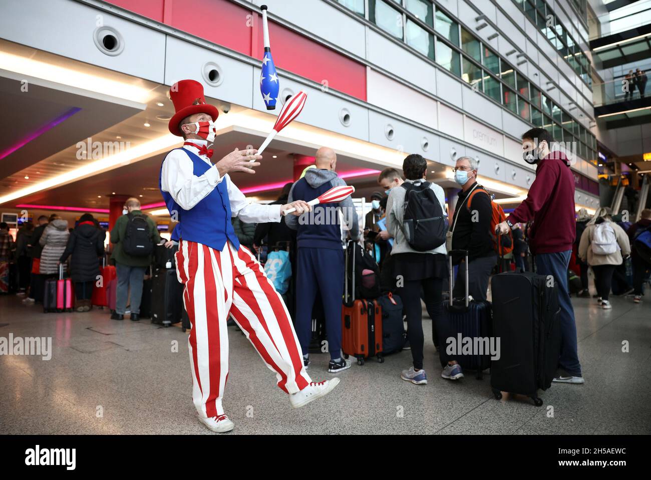 Un intérprete se hace malabarismos mientras se involucra con los viajeros  mientras hacen cola para facturar en los vuelos de Virgin Atlantic y Delta  Air Lines en la terminal 3 del aeropuerto