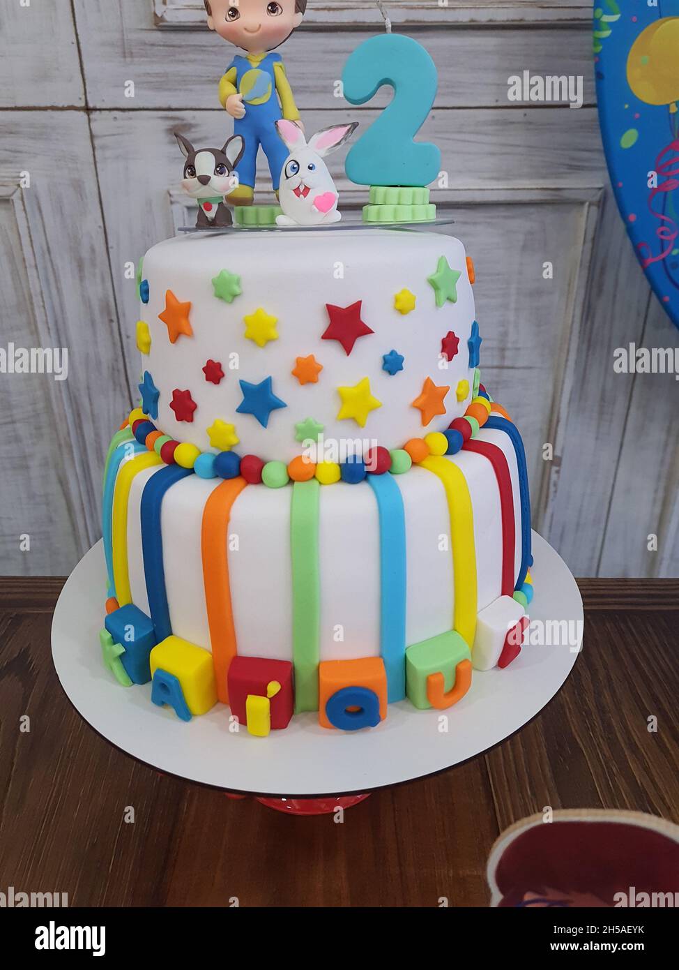 Hermoso pastel de cumpleaños, blanco con decoraciones coloridas, dos pisos  y un niño en miniatura con una vela de 2 años en la parte superior  Fotografía de stock - Alamy