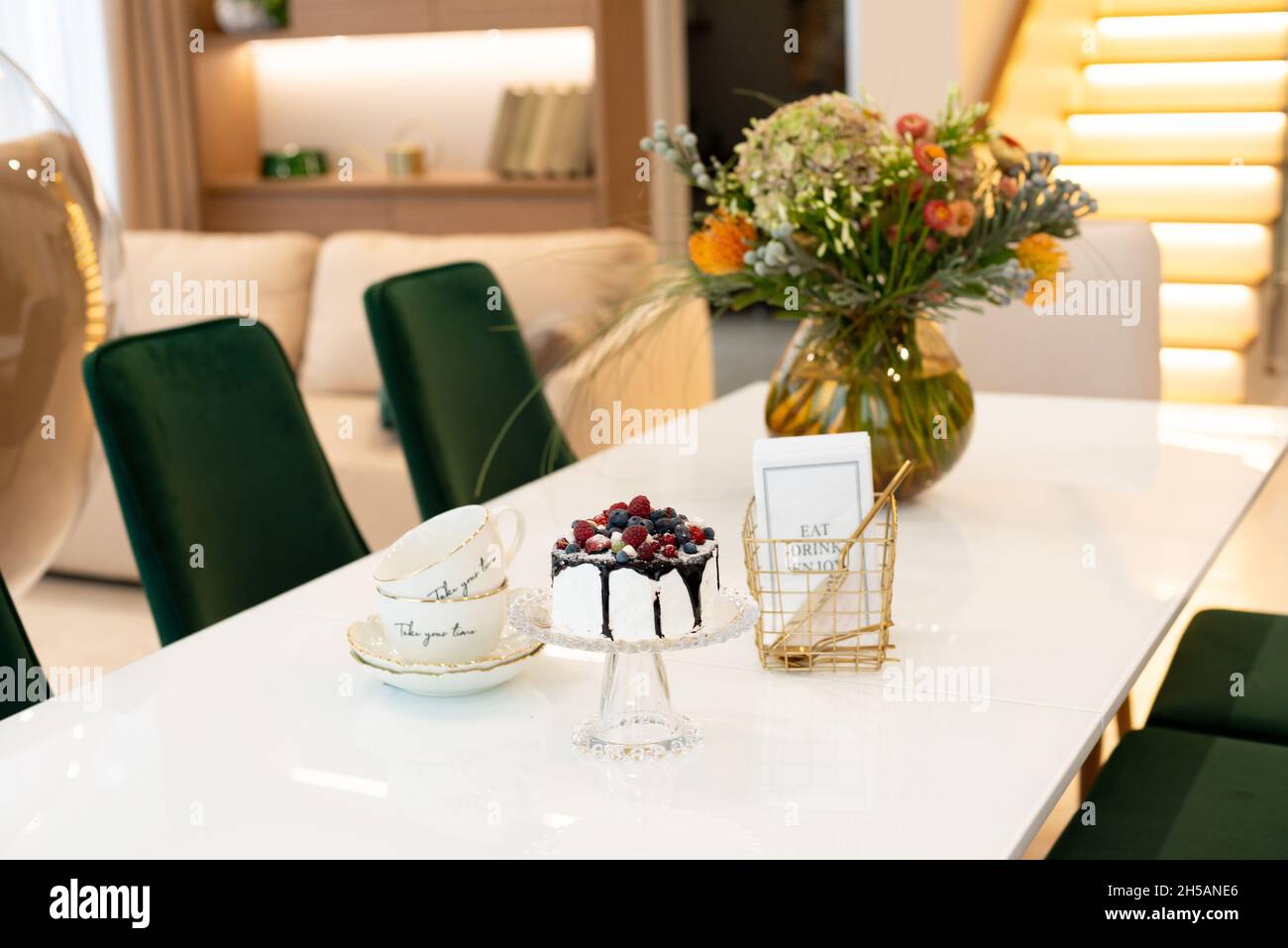 Un exquisito pastel de bayas sobre un soporte de cristal sobre una mesa con un jarrón de flores y un set de té en un moderno diseño interior. Enfoque selectivo suave, art nois Foto de stock