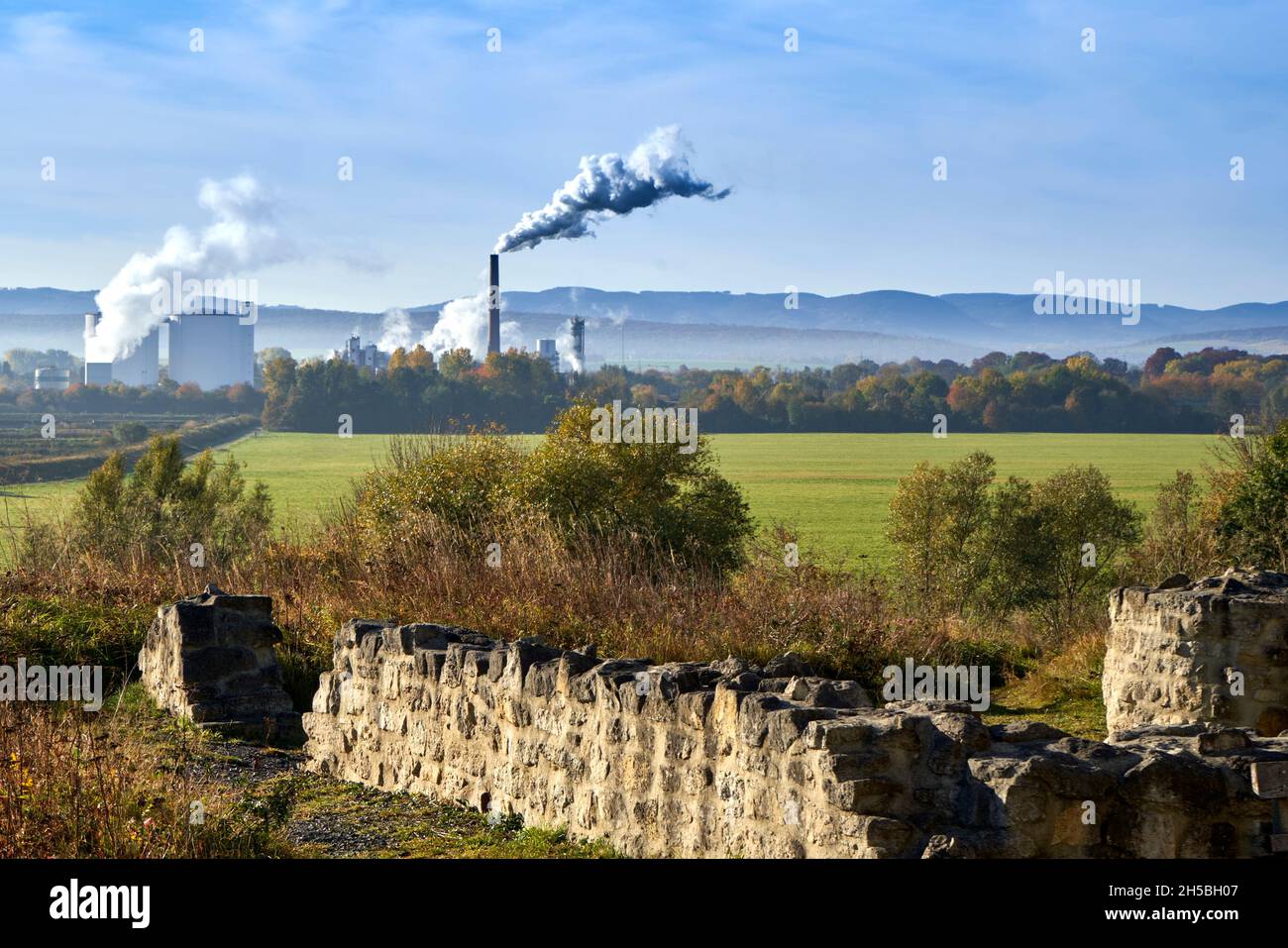 Paredes de una antigua ruina de piedra natural con una fábrica de chimeneas de fumar en el fondo contra la línea de montañas en el horizonte Foto de stock