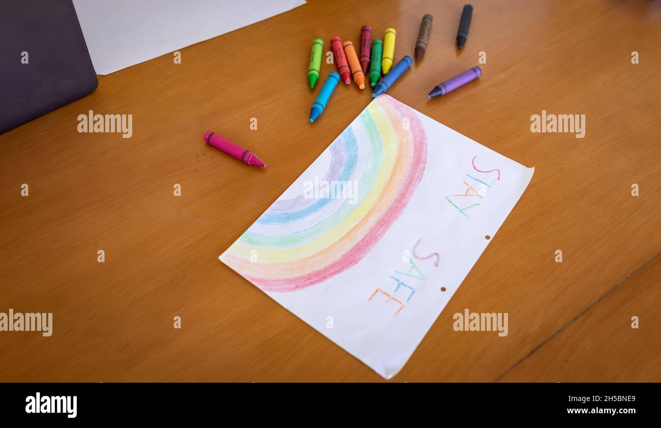 Una pintura de arco iris con un texto Mantente seguro tumbado en una mesa con coloridos lápices de colores tumbados en un metro Foto de stock