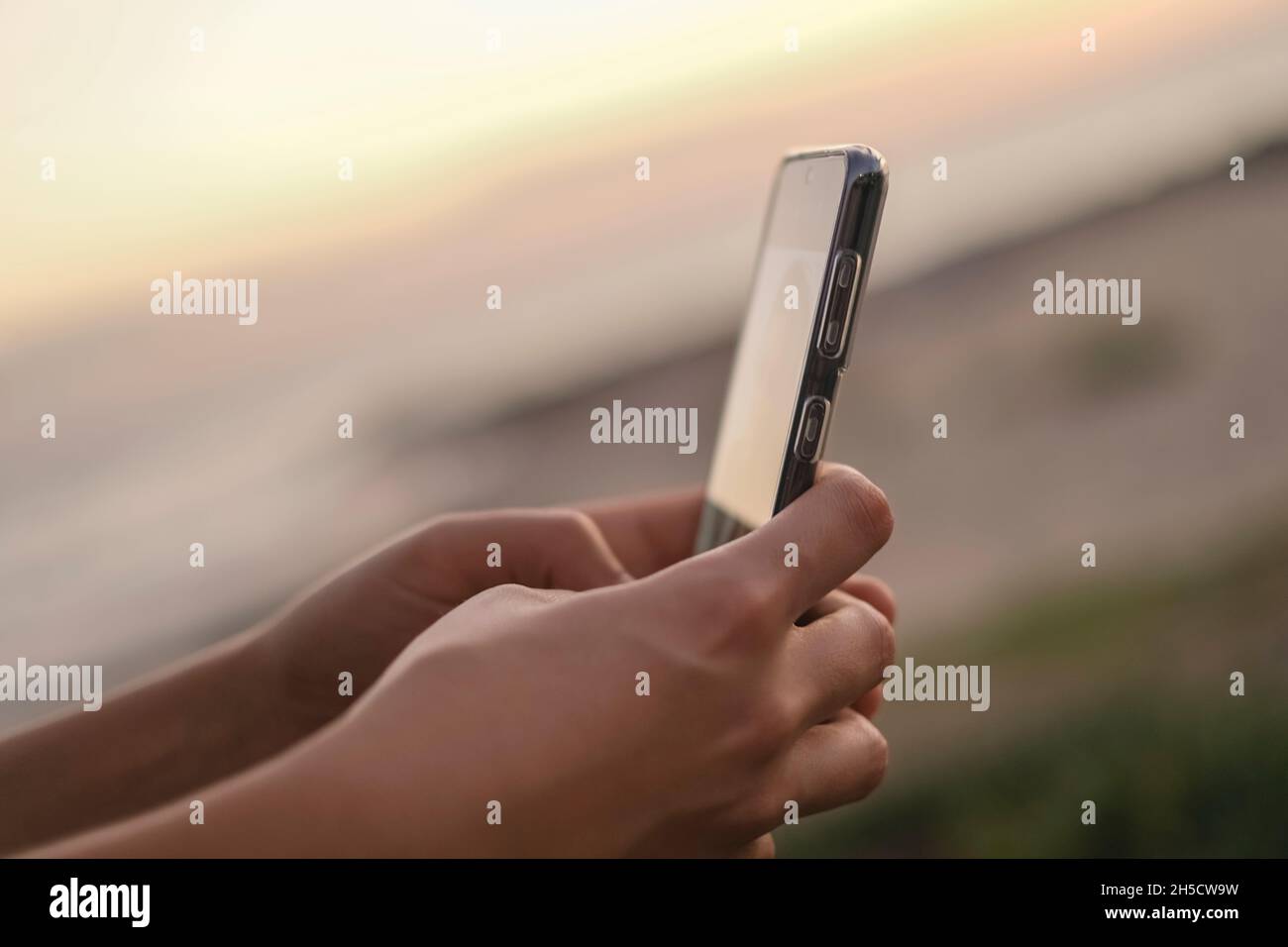 Las mujeres jóvenes utilizan el smartphone para chatear en las redes sociales sobre el fondo de la puesta de sol, la adicción a las células, la tecnología de la nueva era Foto de stock