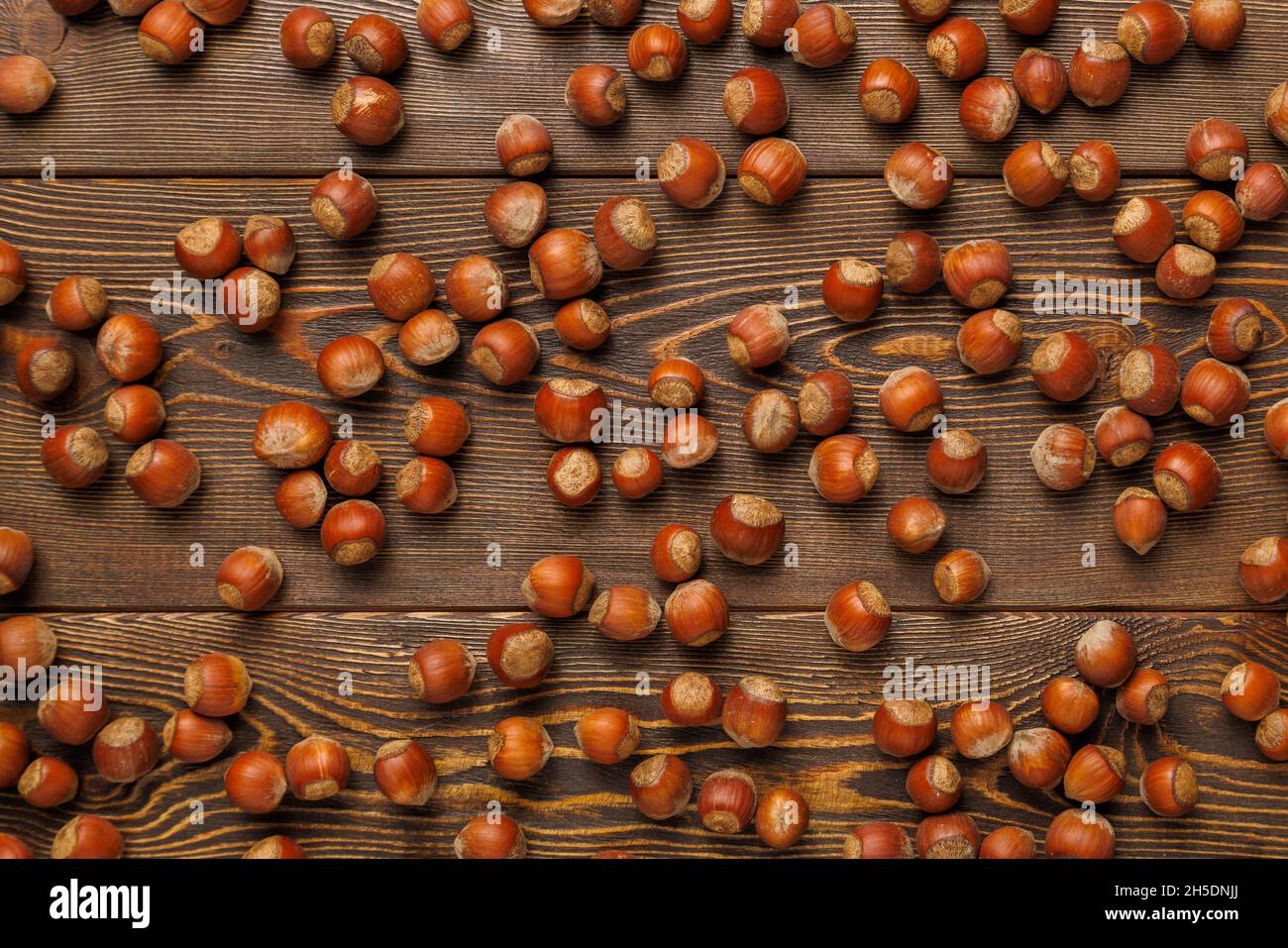 muchas avellanas con cáscaras se extienden uniformemente sobre la superficie de madera marrón Foto de stock