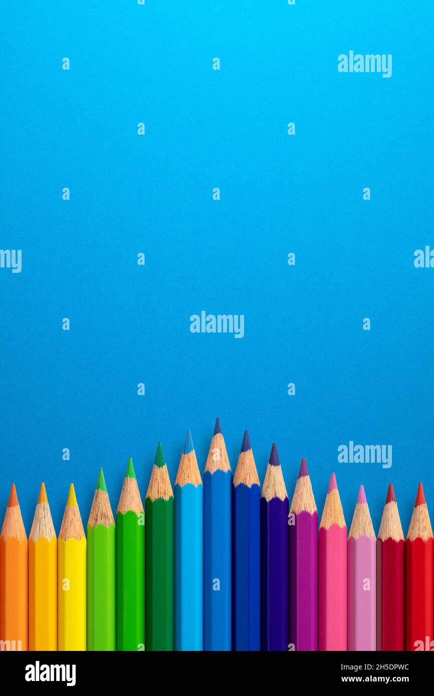 Fondo vertical creativo hecho de lápices de colores sobre papel azul. Capa plana. Concepto de educación. Foto de stock