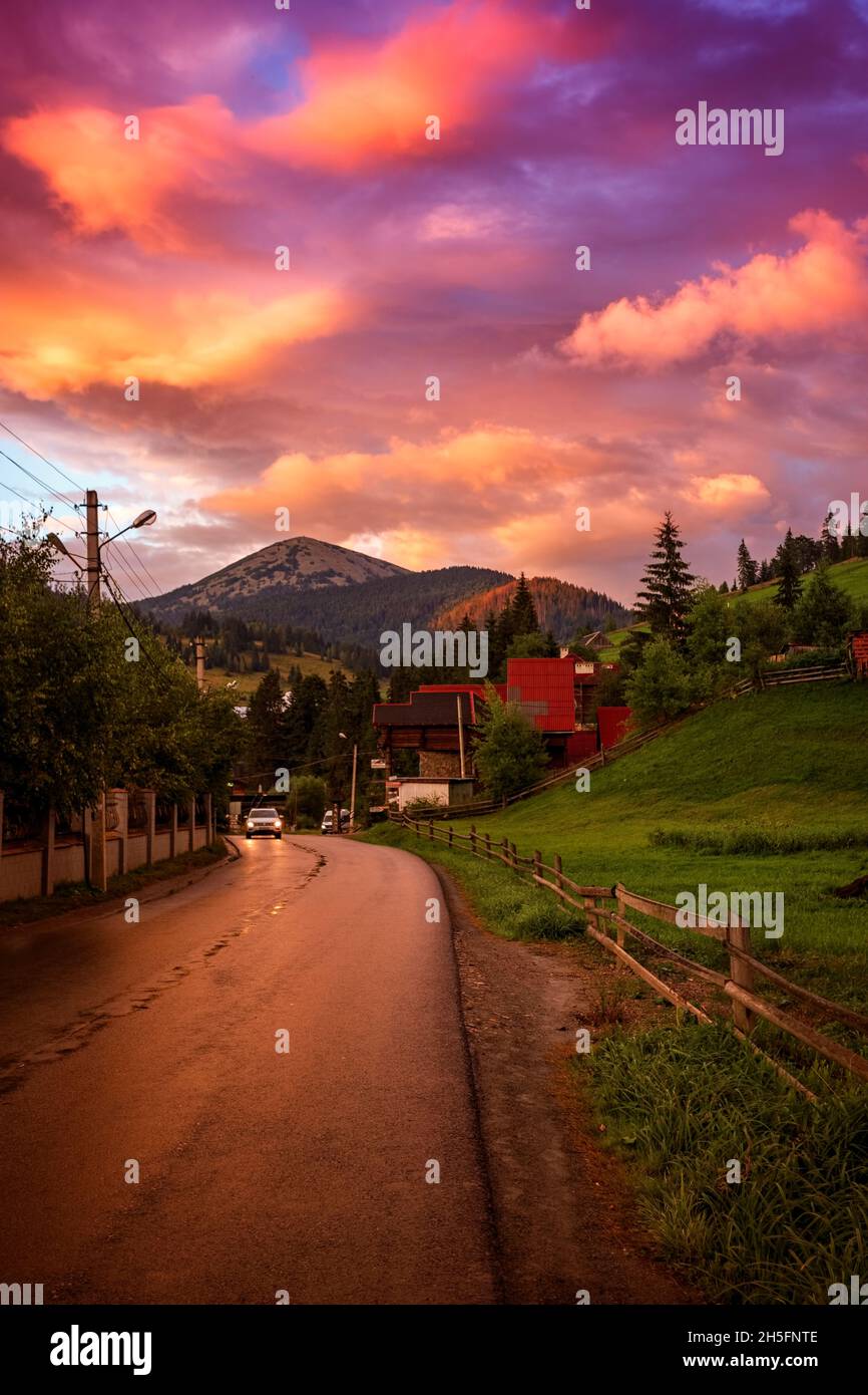 Camino de montaña al atardecer, amanecer, en los Cárpatos, con casas al lado, con una profundidad de campo poco profunda Foto de stock