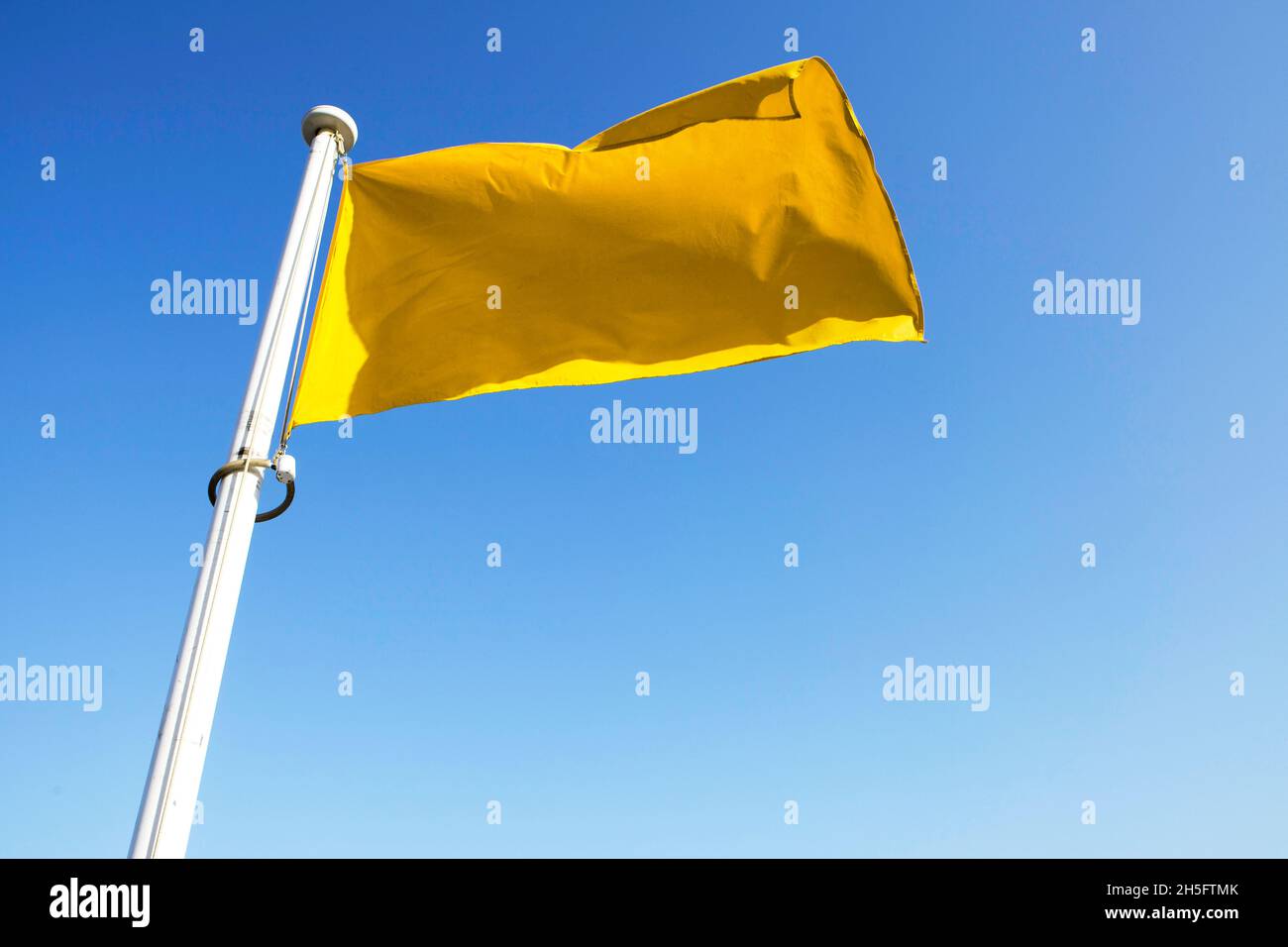 Gelbe Flagge / Fahne, befestigt an einem weißen Masten, weht im Wind vor einem blauen Himmel. Cannes, Frankreich. Foto de stock