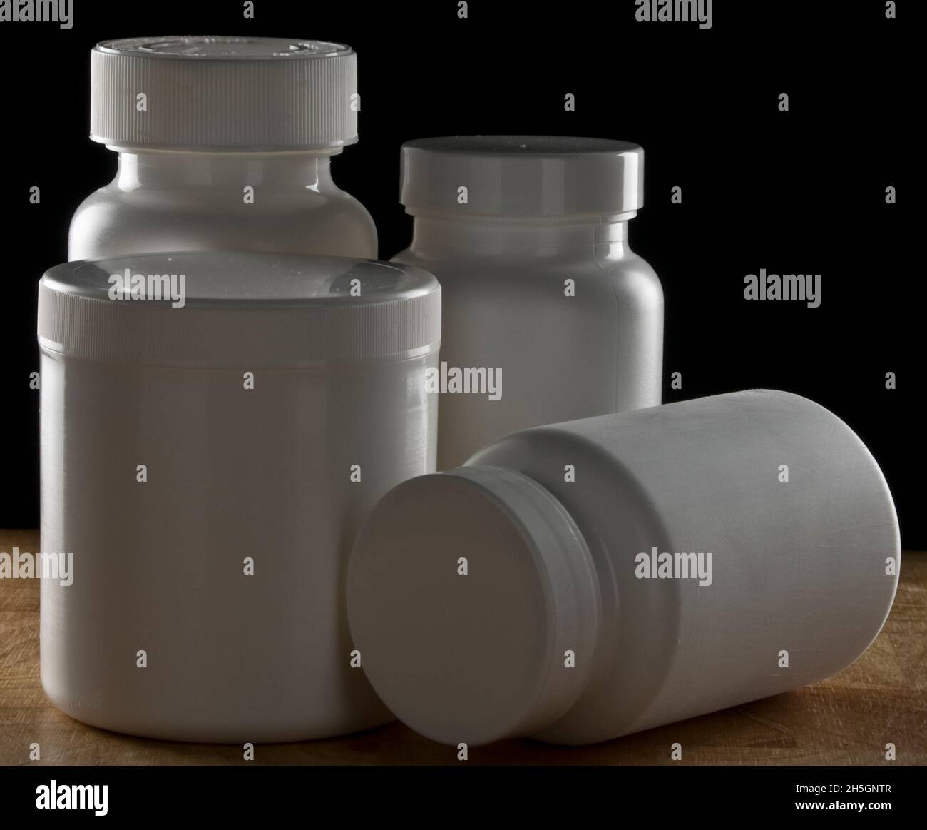 Botellas médicas de la píldora en banco de madera con fondo negro Foto de stock