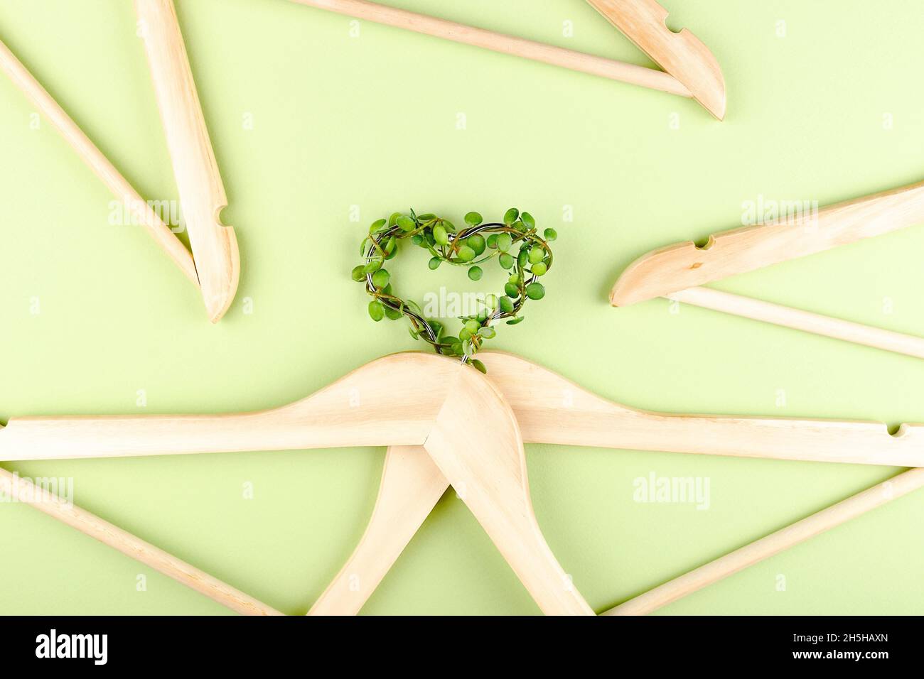 Consumo consciente concepto de moda lenta. Corazón de perchas enredadas con planta sobre fondo verde. Foto de stock