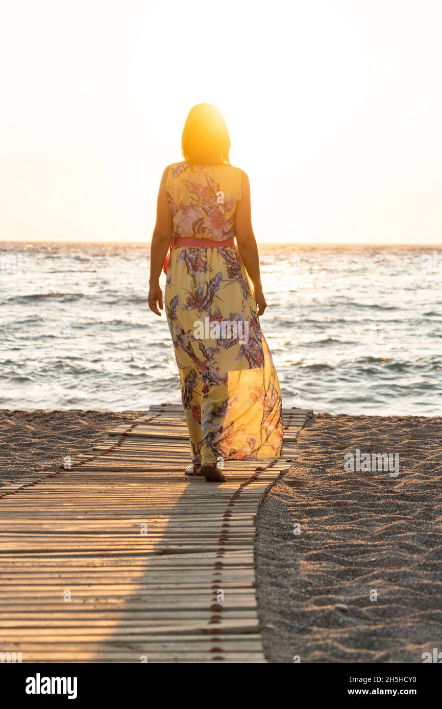 Hermosa mujer con elegante vestido contemplando el mar al atardecer, Matala, Creta, Grecia Foto de stock