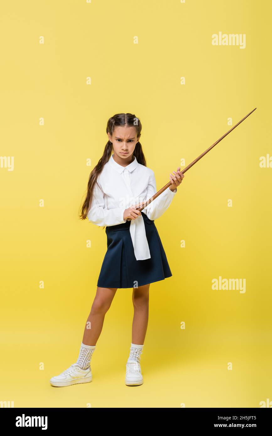 Una niña seria en la falda que sostiene el puntero sobre el fondo amarillo Foto de stock