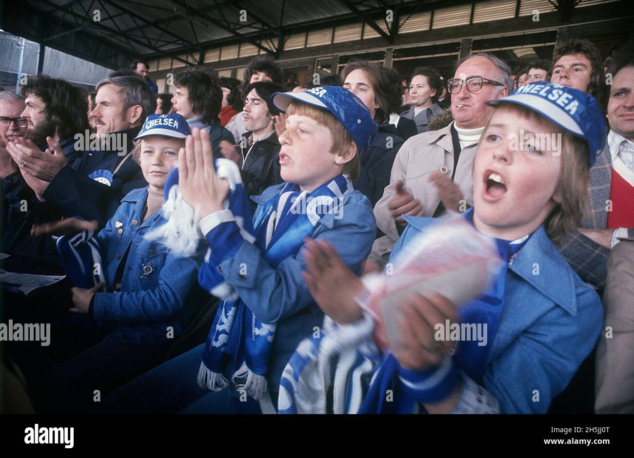 Londres 1982. Tres niños en foco durante un partido de fútbol. Son visiblemente fans de Chelsea con pañuelos y sombreros azules y blancos. Crédito Roland Palm. Foto de stock