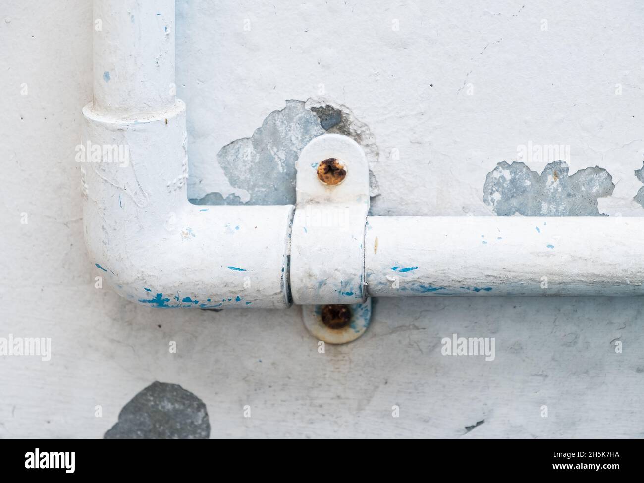 El tubo de PVC con la abrazadera de plástico para el sistema de suministro  de agua en la casa urbana cerca de la pared de concreto blanco, vista  frontal para el espacio