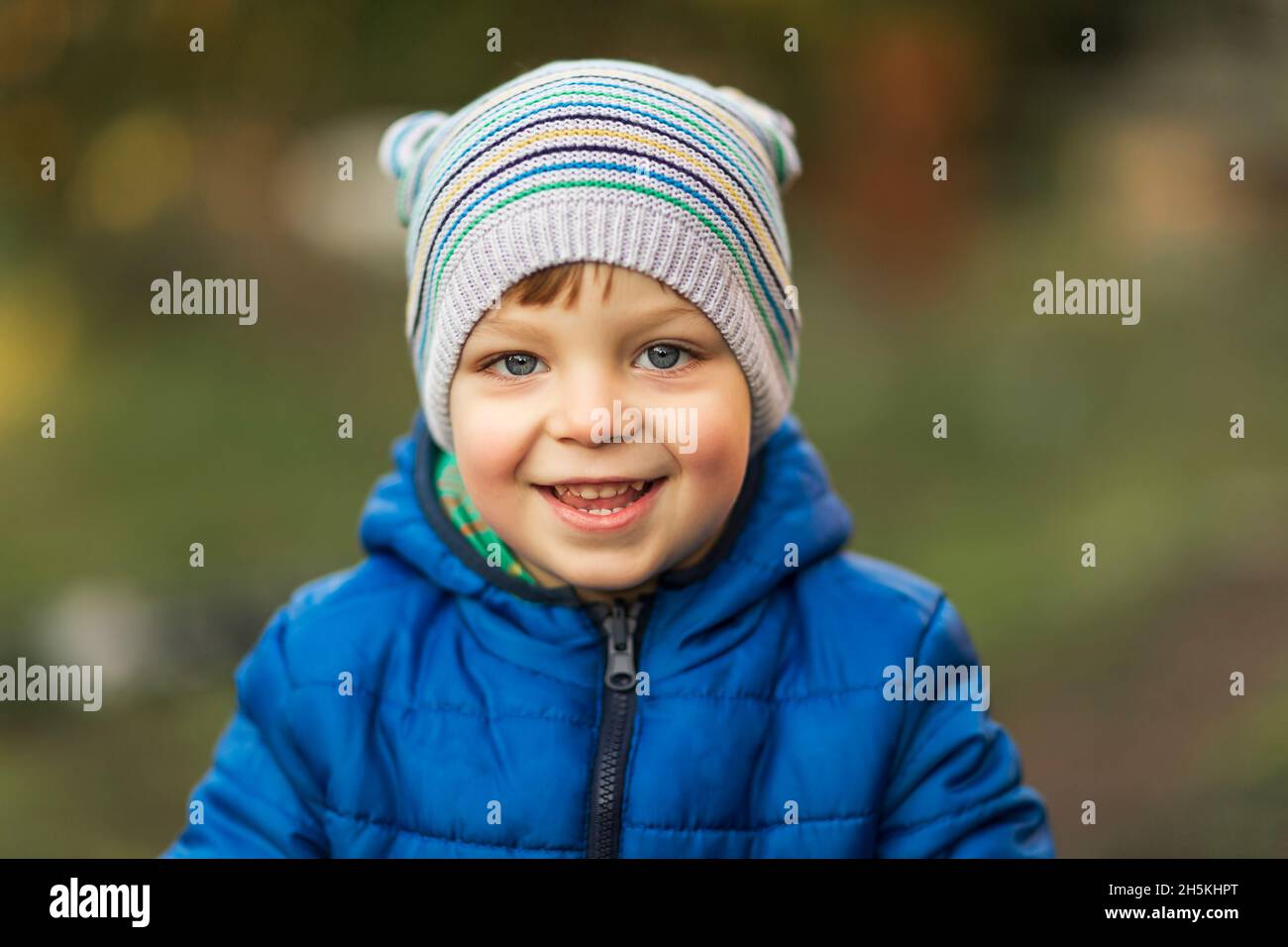 Niño pequeño con ojos azules y chaqueta azul riendo al aire libre Foto de stock
