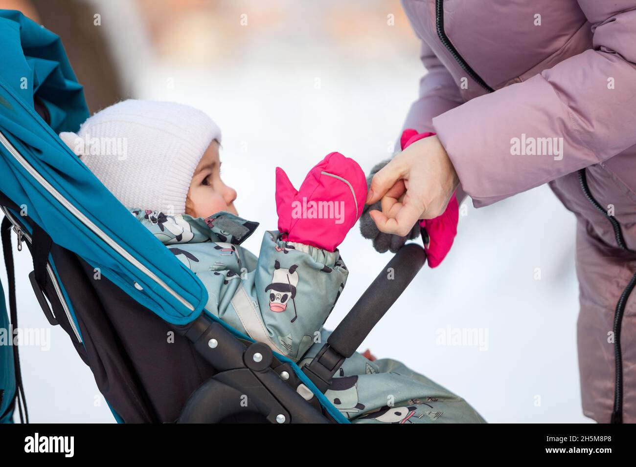 La madre ayuda a usar manoplas rojas en las manos del niño, un bebé sentado en un en la temporada invierno Fotografía de stock - Alamy