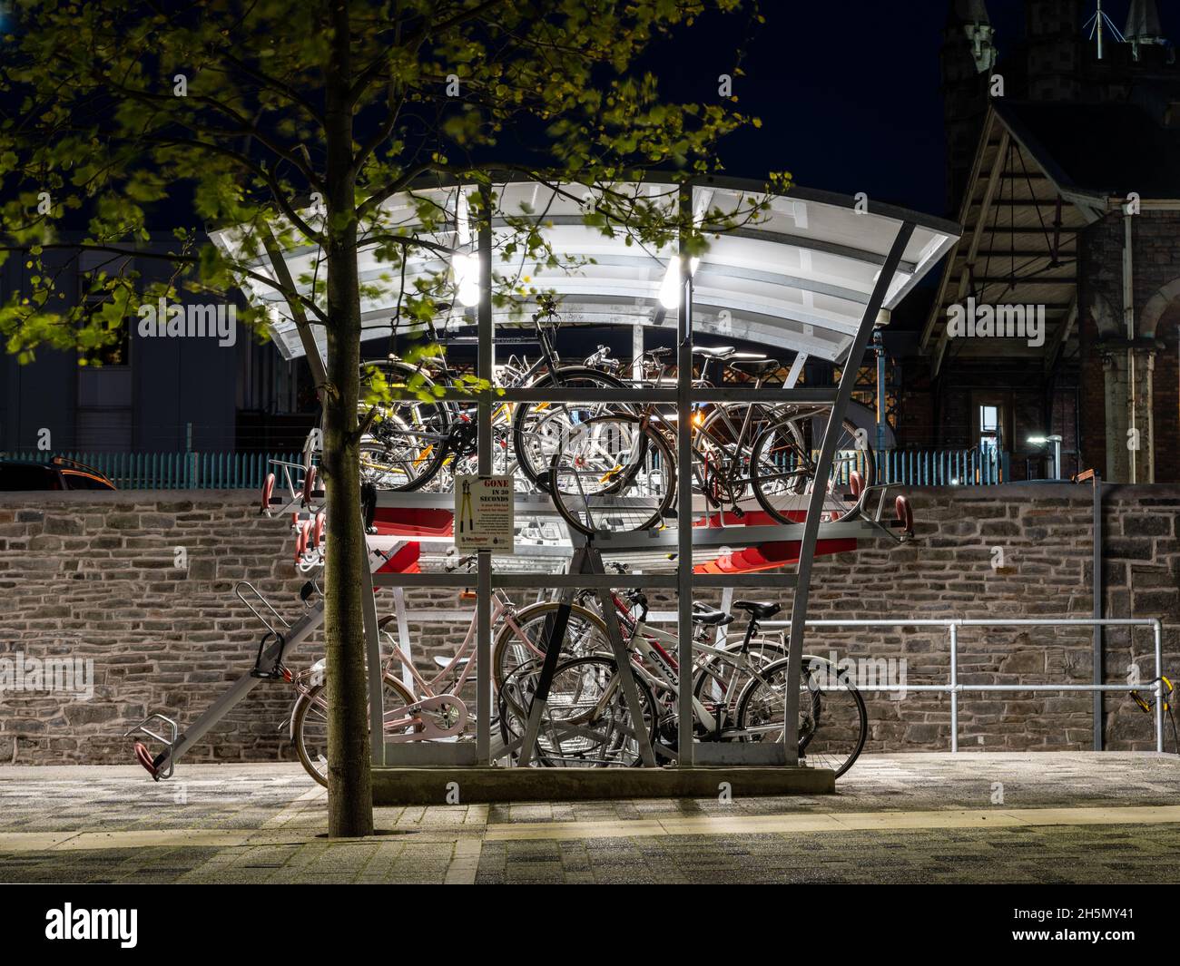 Un refugio de estacionamiento para bicicletas de dos niveles de alta densidad iluminado por la noche en la estación de tren Bristol Temple Meads. Foto de stock