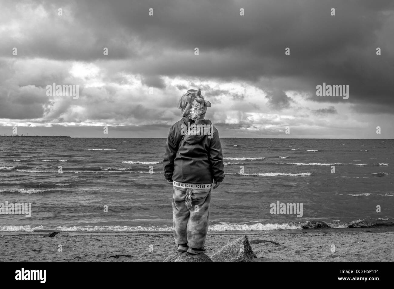 Niña de pie en la orilla del Golfo de Finlandia y mirando al horizonte. Peterhof, San Petersburgo, Rusia. Blanco y negro. Foto de stock