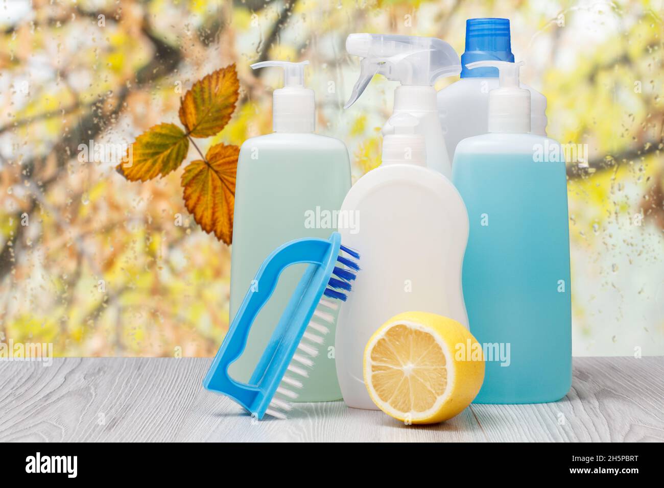 Botellas de plástico de lavavajillas líquido, limpiador de vidrio y  azulejos, detergente para estufas, un brushe y un limón delante de la  ventana con gotas de agua y Fotografía de stock 