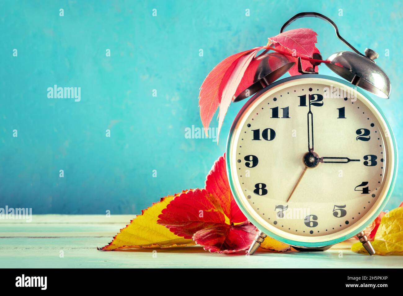 Concepto de horario de verano, DST, otoño atrás en otoño. Un reloj despertador vintage con hojas otoñales sobre un fondo azul con un lugar para el texto Foto de stock