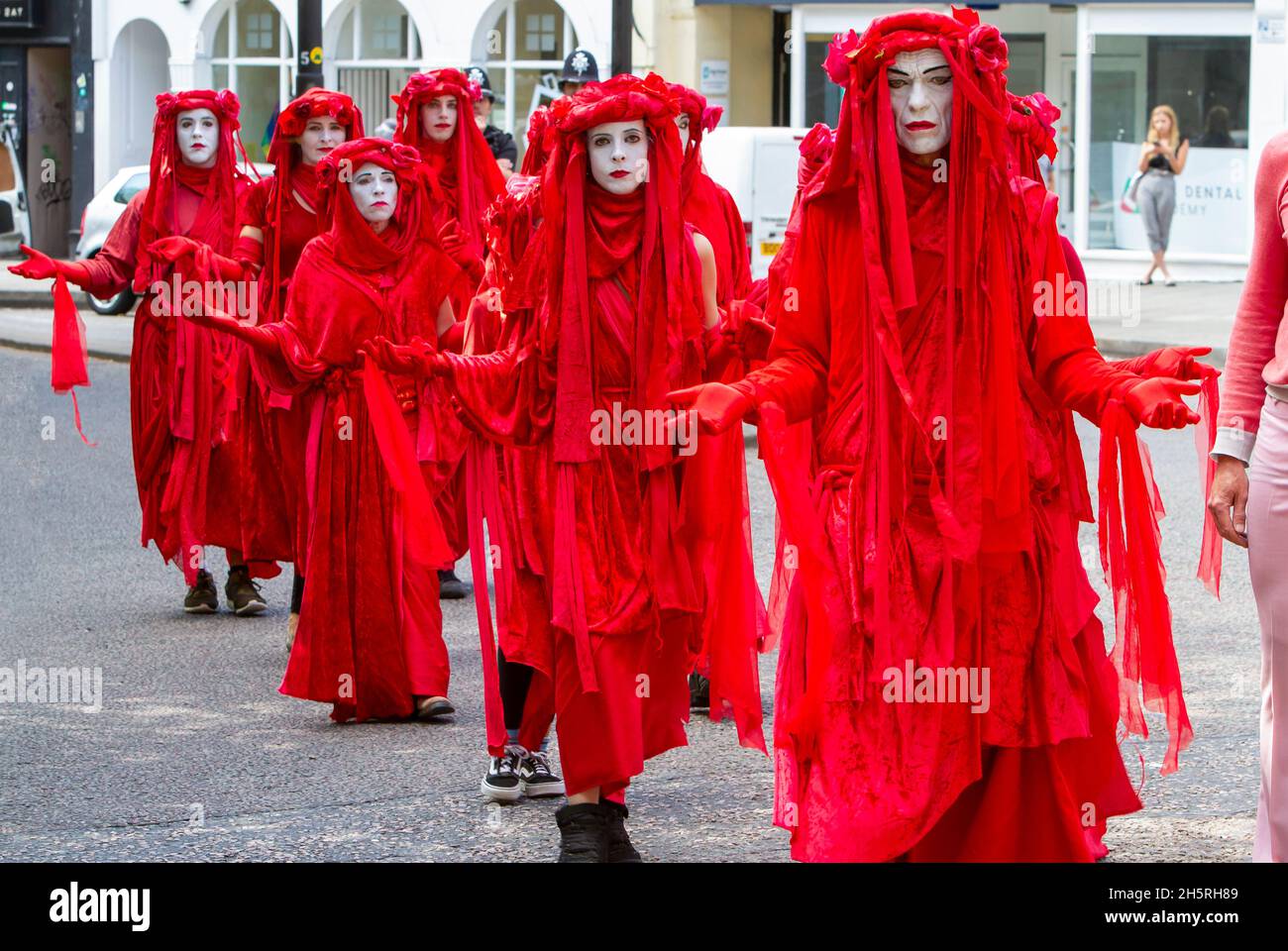 Fotografía de la calle de un grupo de artistas del circo invisible de la Brigada Roja en una demostración de cambio climático que camina en línea por las calles. Foto de stock