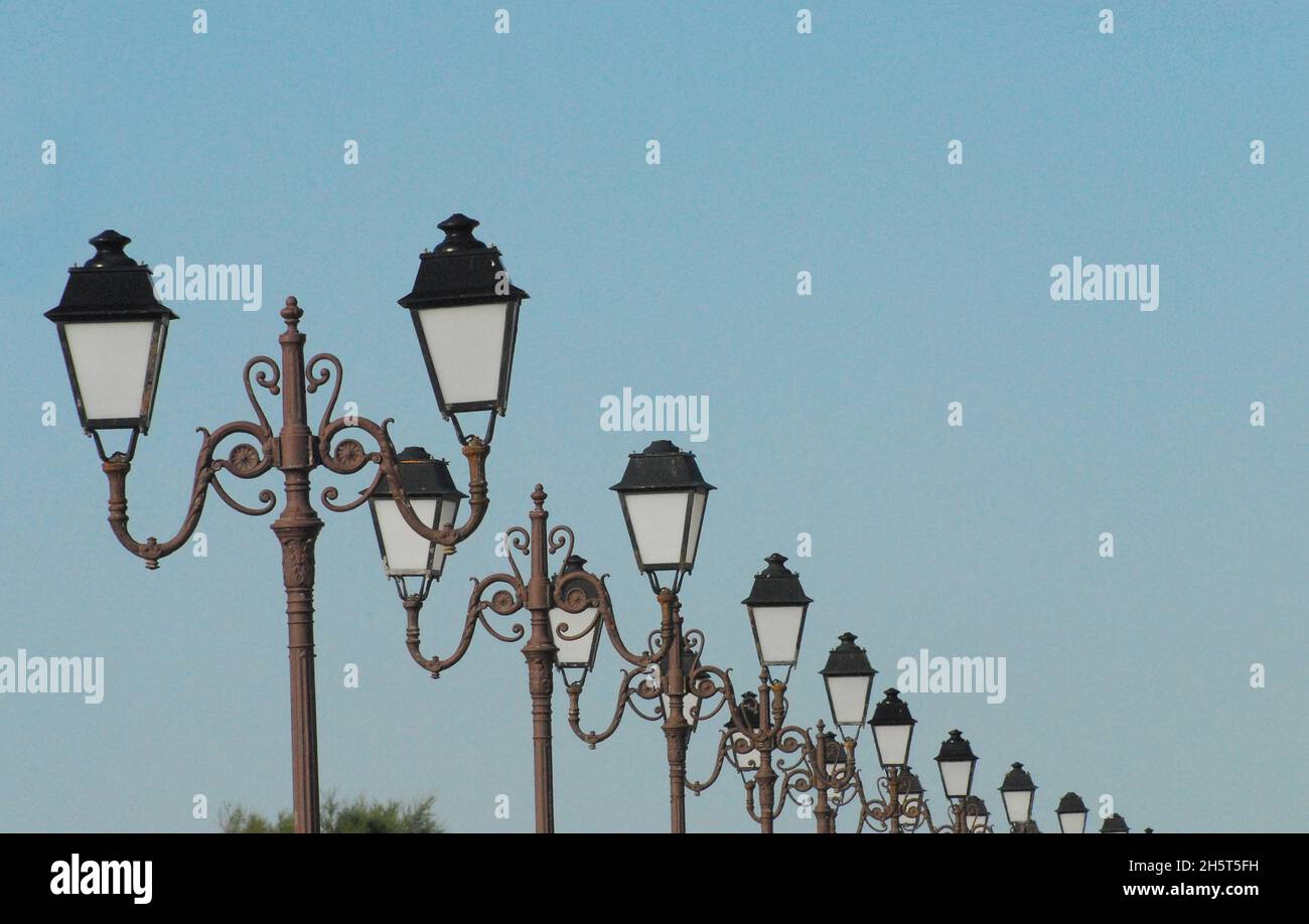 Primer plano de una larga fila de luces de calle ornamentadas en perspectiva decreciente. Rodada en Saintes-Marie-de-la-Mer, Francia. Foto de stock