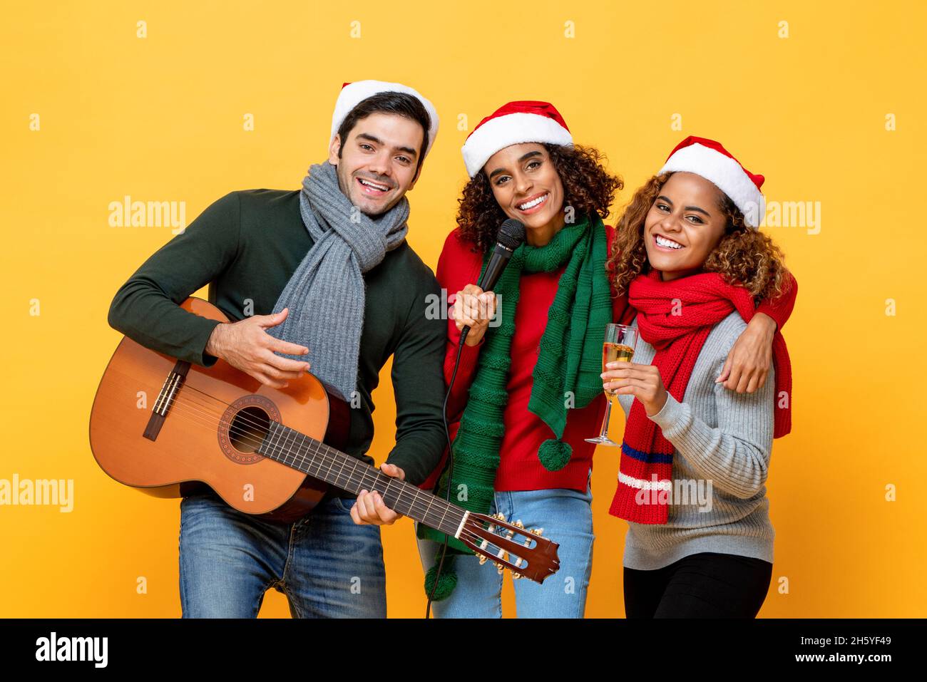 Grupo multiétnico de amigos cercanos que tienen fiesta cantando y celebrando la Navidad en el fondo amarillo estudio aislado Foto de stock