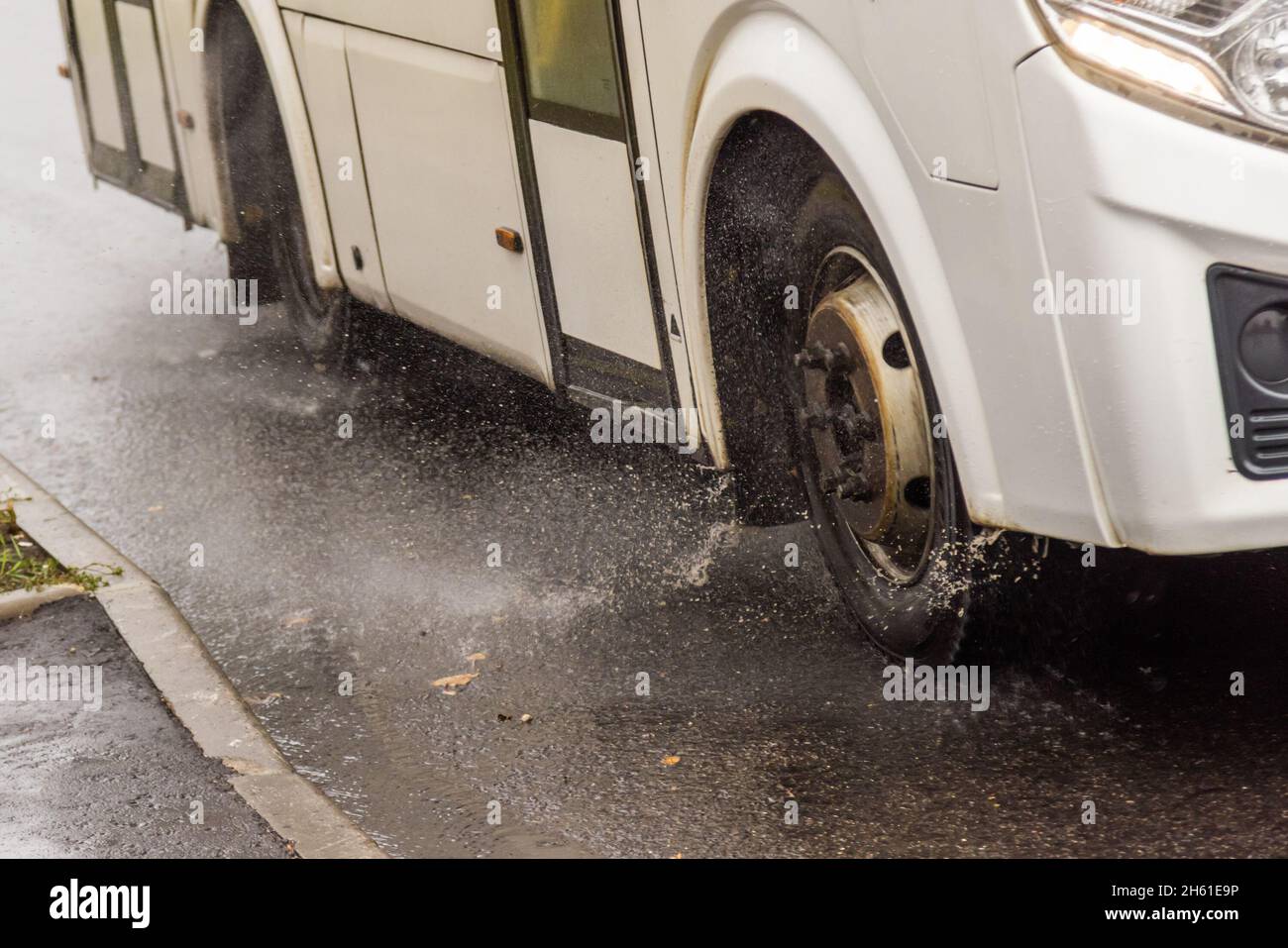 autobús municipal blanco que se mueve en camino lluvioso con salpicaduras de agua Foto de stock