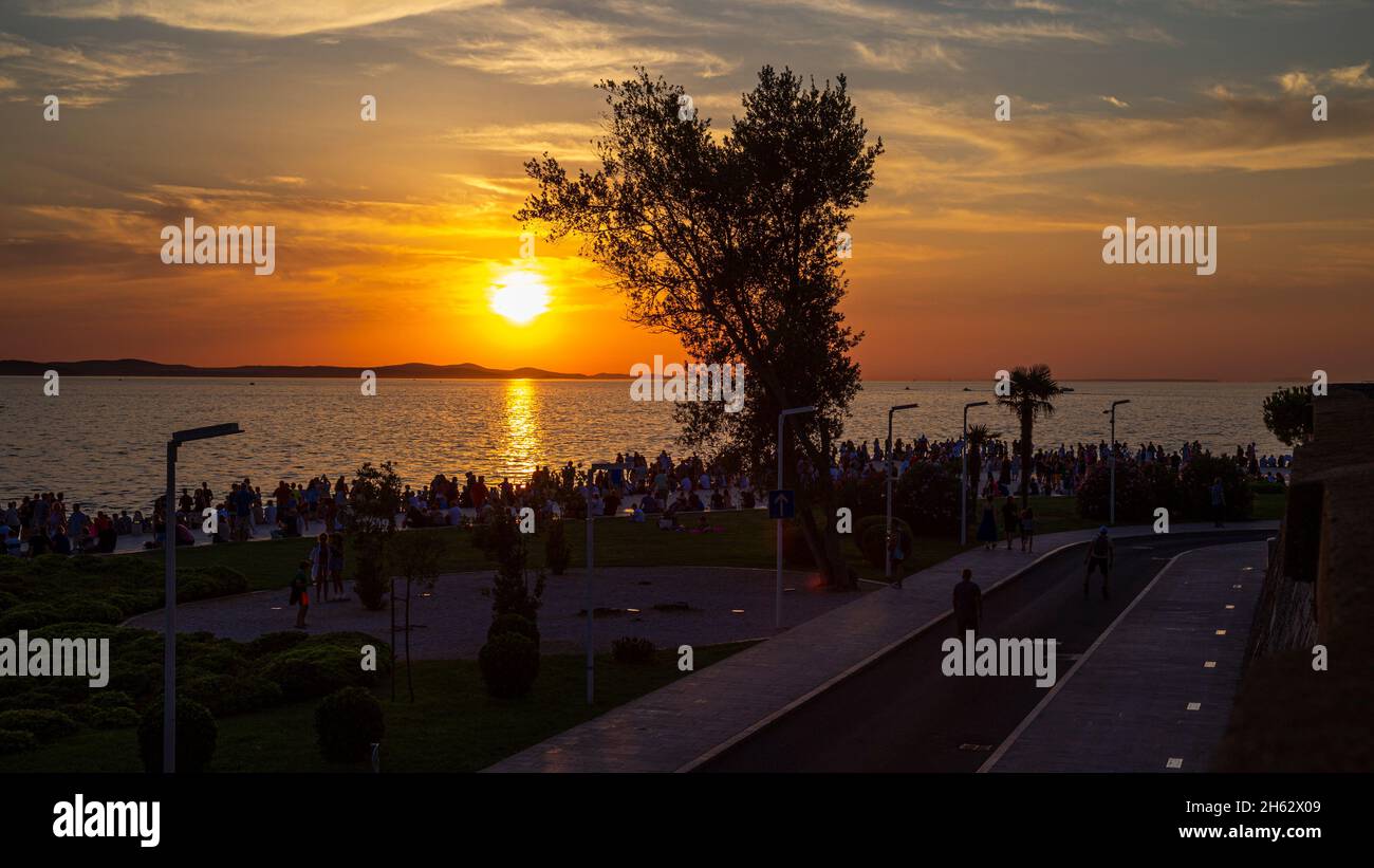 la gente de pie y hacer fotos saludan al sol al atardecer. la playa es famosa por europa, croacia. Foto de stock