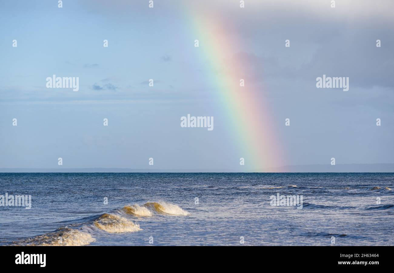 Un hermoso arco iris sobre el océano que termina en el mar y las olas en primer plano. Foto de stock
