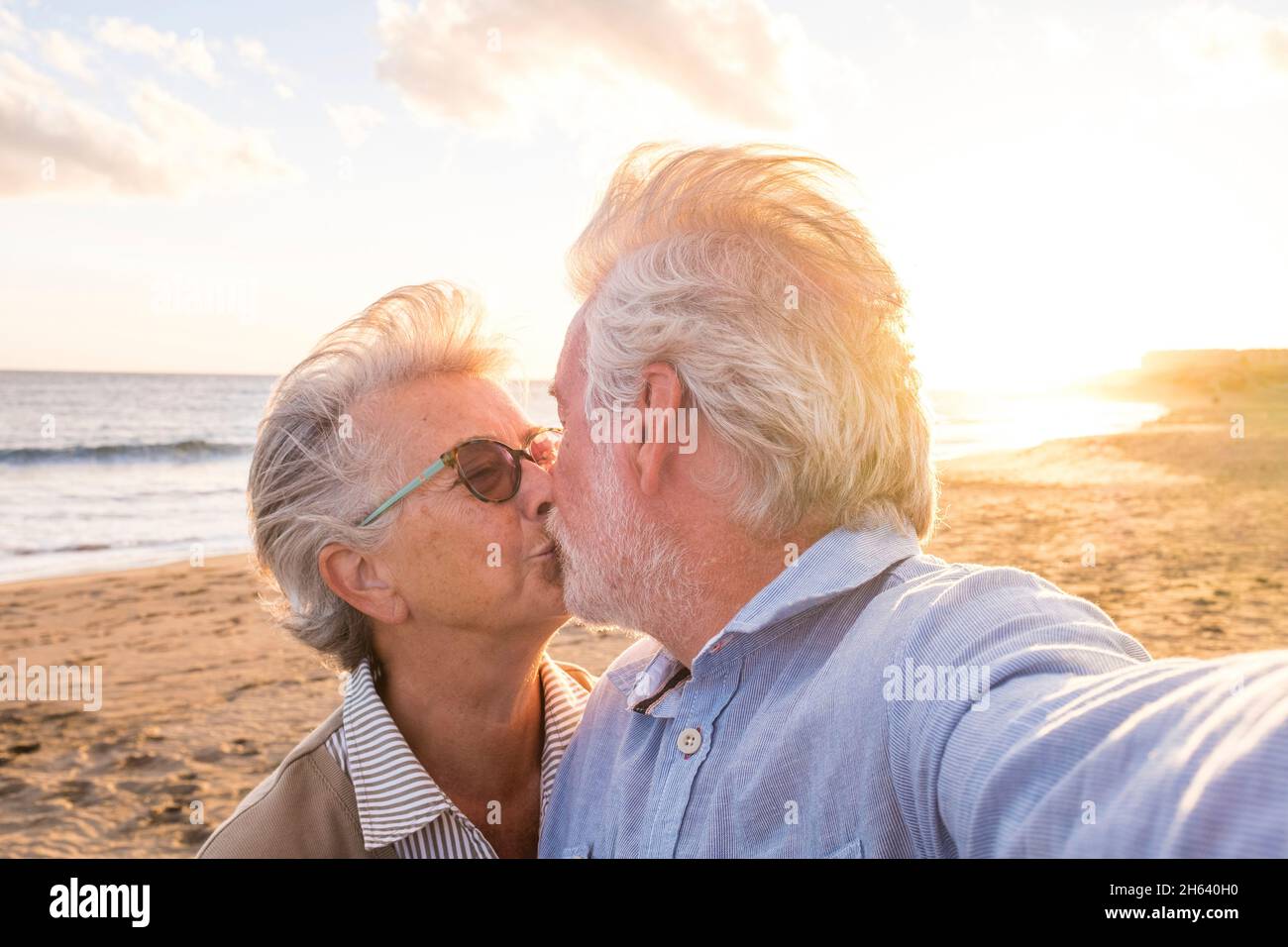retrato de un par de personas mayores y mayores disfrutando del verano en la playa mirando a la cámara tomando un selfie junto con la puesta de sol en el fondo. dos personas mayores activos viajando al aire libre. Foto de stock