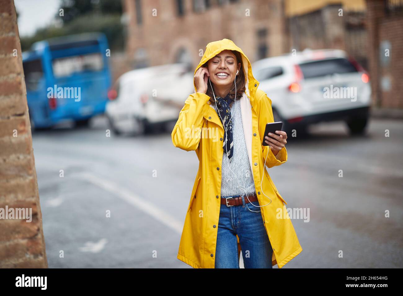 Una niña con chubasquero amarillo disfrutando de la música mientras camina  en un ambiente tranquilo en un día nublado. Paseo, lluvia, ciudad  Fotografía de stock - Alamy