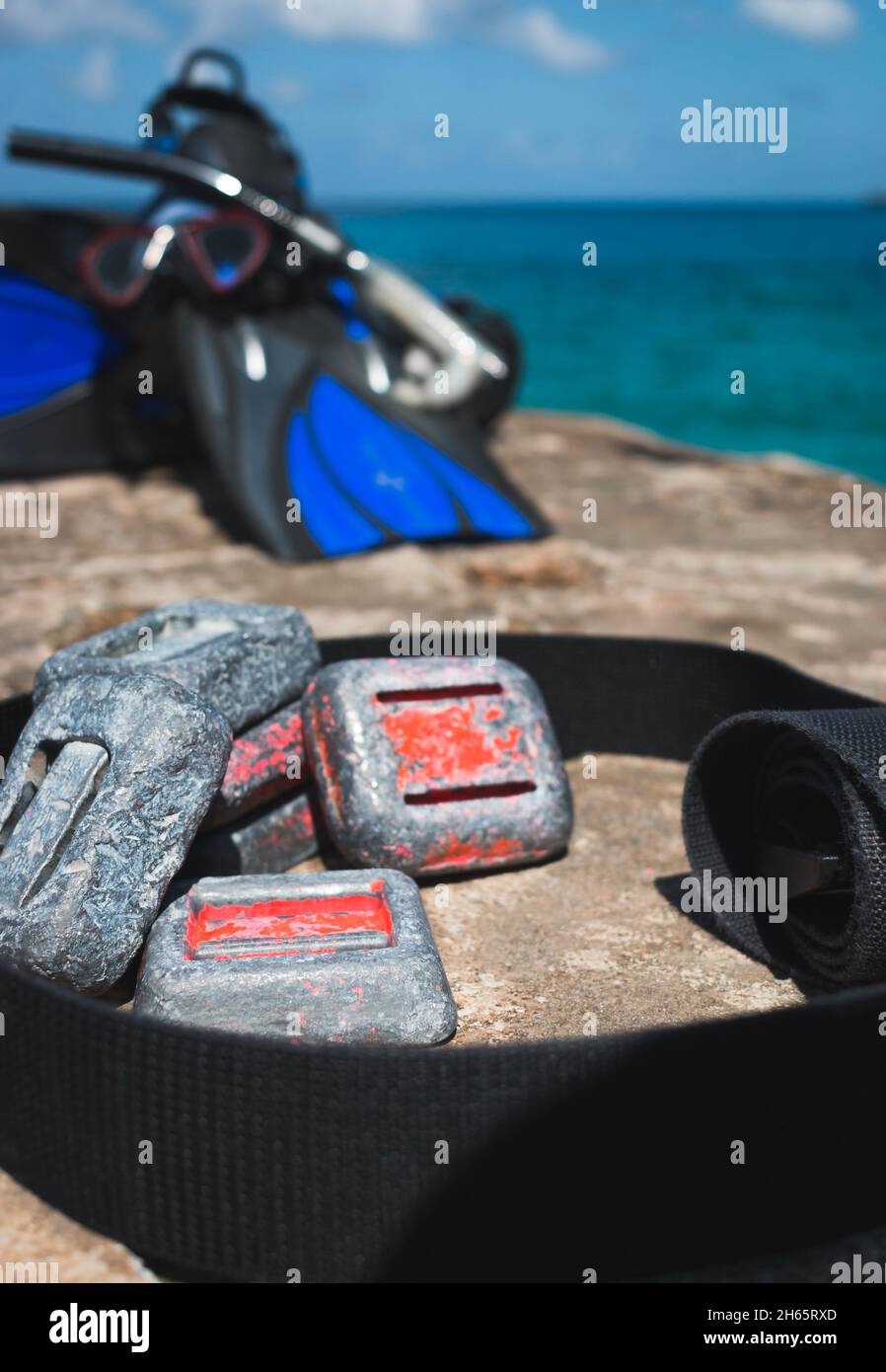 Pesas de buceo en roca junto al océano con equipo de esnórquel en el fondo Foto de stock