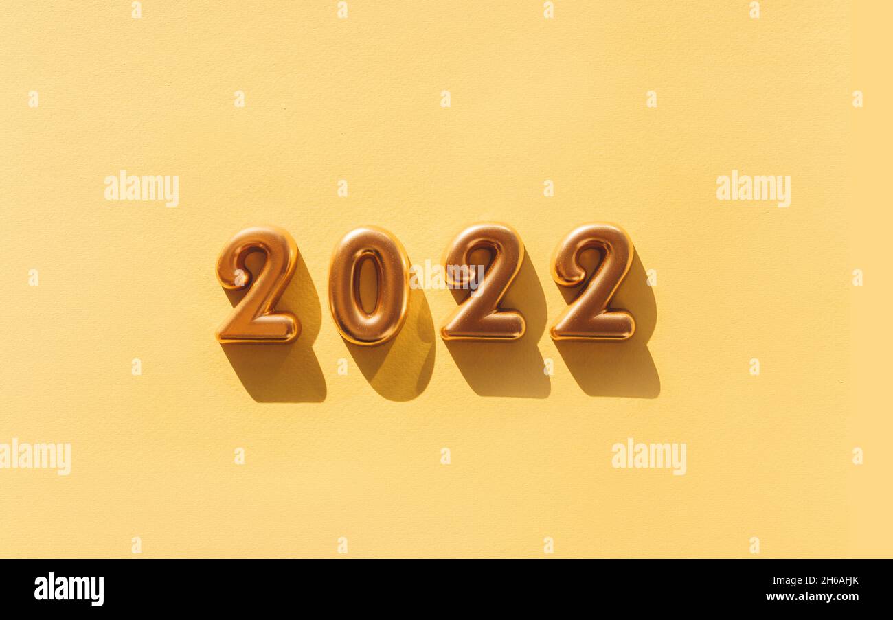 Globos hechos de papel de aluminio dorado con los números 2022 sobre fondo dorado. Celebración de Navidad, Año Nuevo y el concepto de vacaciones. Plano, vista superior. Foto de stock