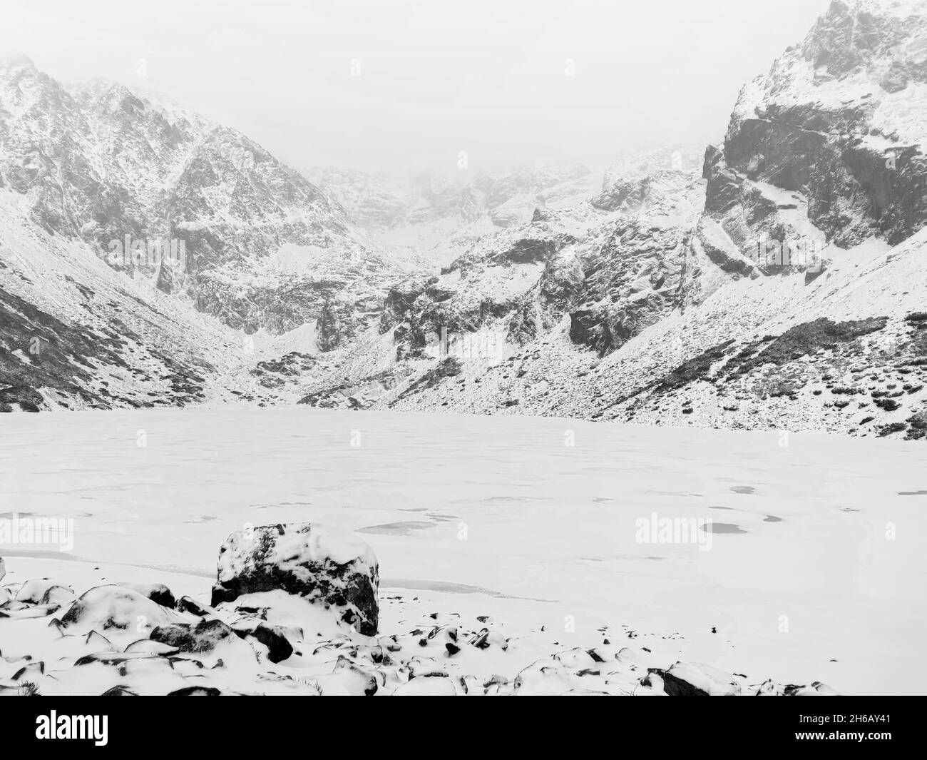 Una vista panorámica en escala de grises de terreno abierto con rocas cubiertas de nieve y montañas en el fondo Foto de stock