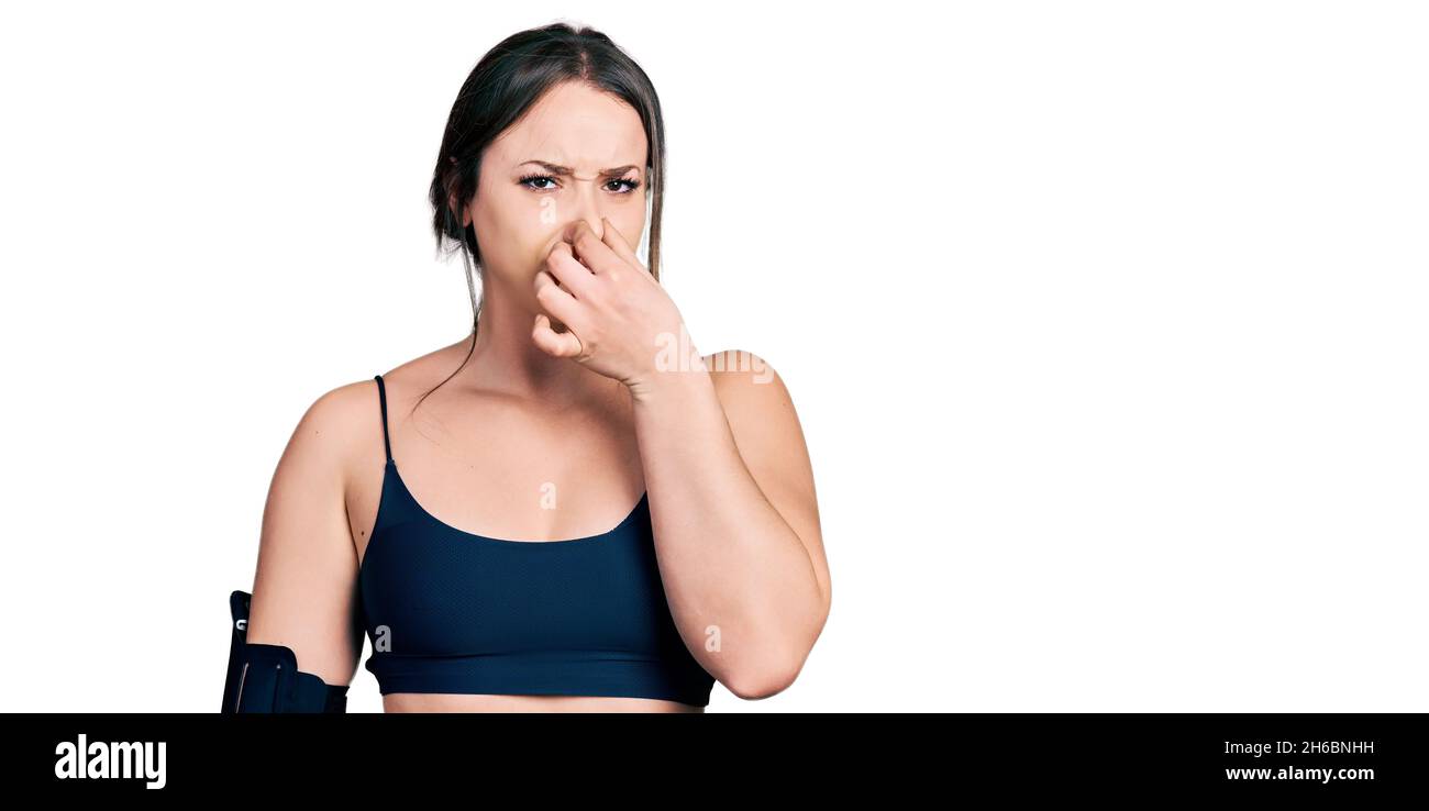 Mujer hispana joven usando ropa deportiva oliendo algo apestoso y  desagradable, olor intolerable, sosteniendo el aliento con los dedos en la  nariz. Mal olor Fotografía de stock - Alamy