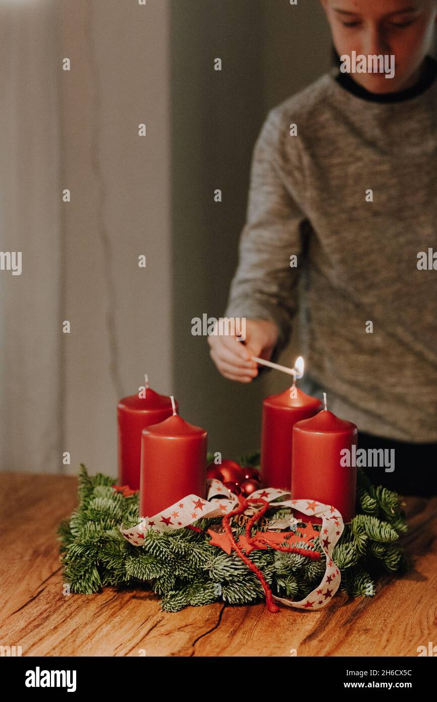Niño adolescente encendiendo la primera vela de Adviento Wreath en el primer domingo de Adviento contando cuatro semanas hasta Navidad. Antigua tradición suiza en Decemb Foto de stock