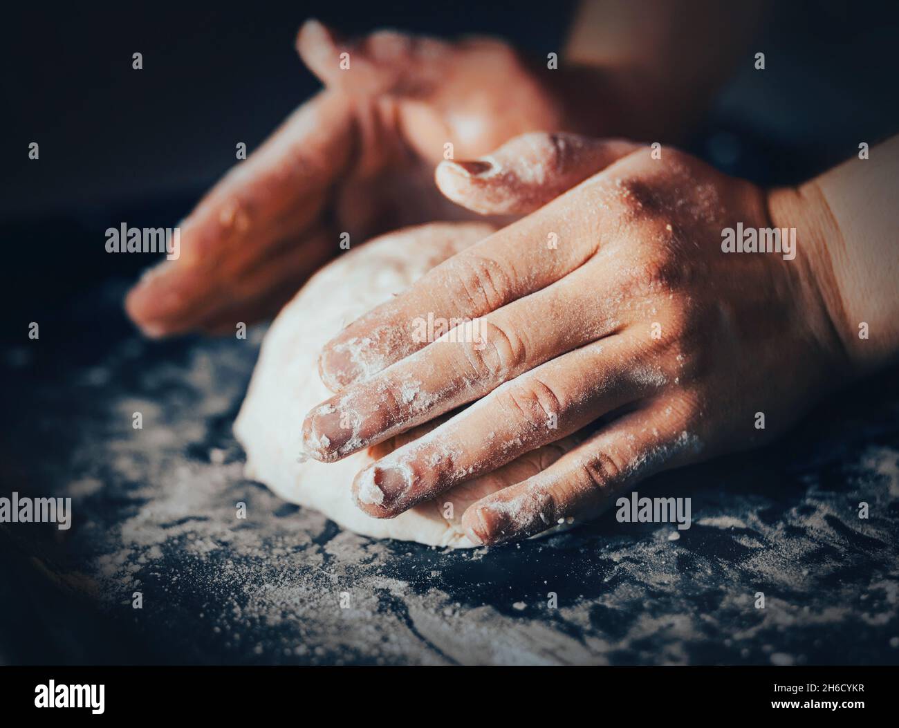 Un hombre amasa la masa con las manos en una hoja de hornear. El proceso de hacer masa de pan. Horneado y cocina casera. Fotos de alimentos Foto de stock