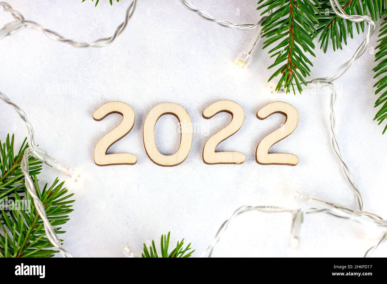 La silueta de los números 2022 de madera con luces de Navidad y ramas verdes de abetos sobre fondo claro. Comienzo de Año Nuevo felicitaciones y planificación Foto de stock