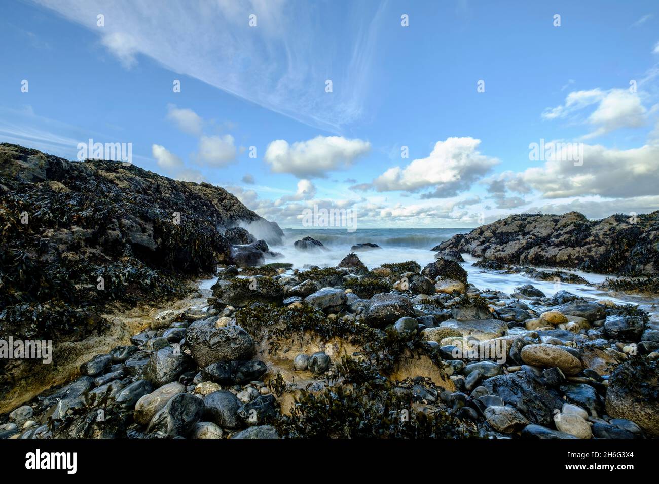 Una vista en ángulo bajo de las olas rompiendo sobre las rocas en Penmon Point en Anglesey, Gales del Norte, Reino Unido Foto de stock